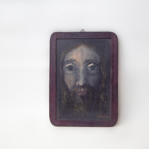 May include: A framed painting of a man's face with a beard and long hair. The painting is done in a dark, muted color palette and the man's eyes are looking directly at the viewer.