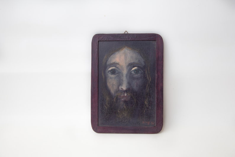 May include: A framed painting of a man's face with a beard and long hair. The painting is done in a dark, muted color palette and the man's eyes are looking directly at the viewer.