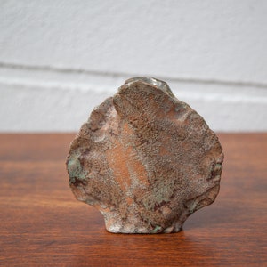 K&ouml;nnte beinhalten: Eine handgefertigte, abstrakte Keramikskulptur mit rauer, strukturierter Oberfl&auml;che. Die Skulptur weist eine Mischung aus Erdt&ouml;nen auf, darunter Braun und gr&uuml;ne Akzente, wodurch eine einzigartige, organische &Auml;sthetik entsteht. Das St&uuml;ck wird auf einer Holzoberfl&auml;che pr&auml;sentiert.