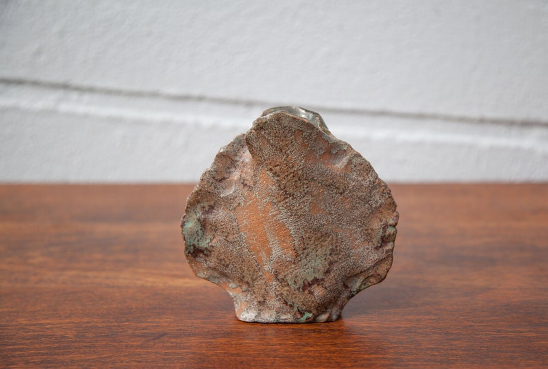 K&ouml;nnte beinhalten: Eine handgefertigte, abstrakte Keramikskulptur mit rauer, strukturierter Oberfl&auml;che. Die Skulptur weist eine Mischung aus Erdt&ouml;nen auf, darunter Braun und gr&uuml;ne Akzente, wodurch eine einzigartige, organische &Auml;sthetik entsteht. Das St&uuml;ck wird auf einer Holzoberfl&auml;che pr&auml;sentiert.