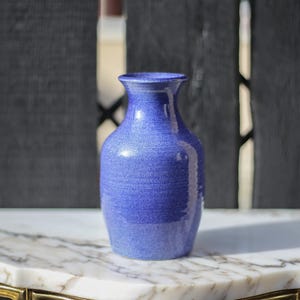 Könnte beinhalten: Eine blaue Keramikvase mit strukturierter Oberfläche. Die Vase steht auf einer weißen Marmorfläche.