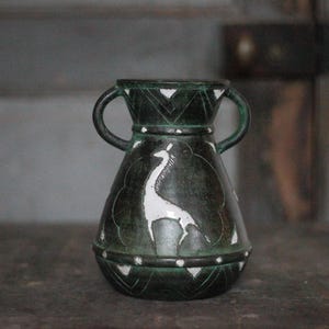 Op de afbeelding: Een donkergroene keramische vaas met twee handvatten en een wit giraffedesign. De vaas heeft een bolvorm met een smalle hals en is versierd met geometrische patronen. De vaas is ongeveer 15 cm hoog.