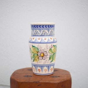 Peut inclure: Un vase en céramique blanche avec un motif floral. Le vase a une bordure bleue et blanche avec un motif floral dans les tons de vert, jaune et violet.