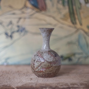 Peut inclure: Un petit vase rond en céramique avec un glaçage brun et blanc. Le vase présente un motif floral dans les tons bruns et rouges.