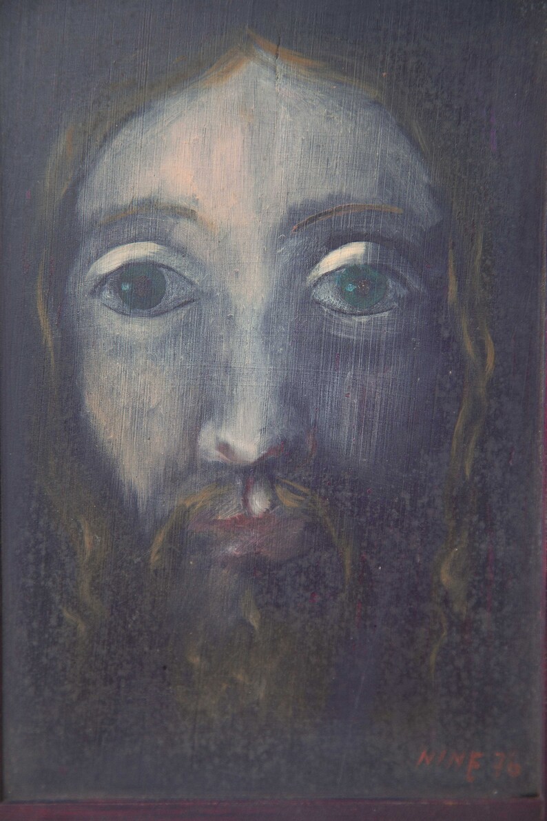 May include: A painting of a person with long, dark hair and a beard. The person has a light blue face with green eyes and a light pink mouth. The painting is on a dark background and has the signature "NIME 76" in the bottom right corner.