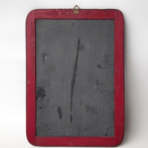 May include: A vintage slate chalkboard with a red wooden frame and a brass hook. The chalkboard has a dark gray surface with some marks and scratches.