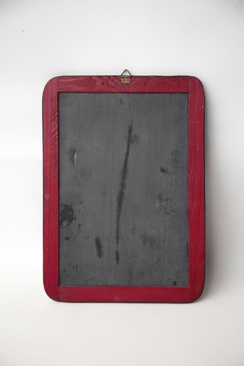 May include: A vintage slate chalkboard with a red wooden frame and a brass hook. The chalkboard has a dark gray surface with some marks and scratches.