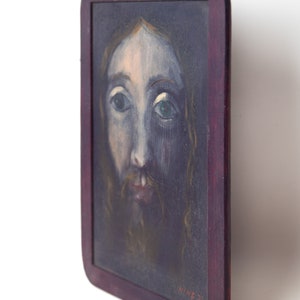 May include: A framed painting of a man's face with a beard and long hair. The painting is done in a dark blue and brown color scheme. The frame is dark wood with a red stain. The painting is signed "HINE 76" in the lower right corner.