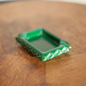 Könnte beinhalten: Ein grüner Aschenbecher aus Glas mit geometrischem Design. Der Aschenbecher steht auf einer Holzoberfläche.
