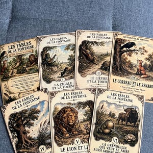 Peut inclure: Un ensemble de sept cartes rectangulaires intitulées Les Fables de La Fontaine, illustrées de scènes classiques. Les cartes représentent des animaux tels qu'un lion, un renard, un corbeau, une tortue, un lièvre et une grenouille avec du texte.