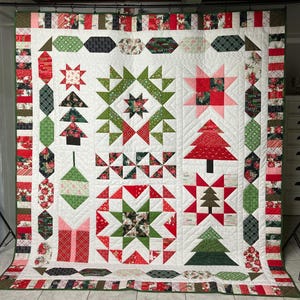 May include: A large, handmade Christmas quilt with a white background and various festive designs. The quilt features red, green, and white geometric shapes, stars, Christmas trees, and gift box patterns. The border includes floral and striped patterns.