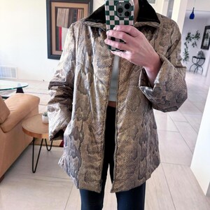 May include: A tan and gray snakeskin-patterned jacket with a black collar. The jacket has a zipper closure and long sleeves. The jacket is a neutral color and could be worn in the fall or winter.