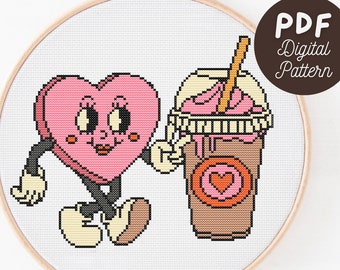 Puede incluir: Patrón de punto de cruz con un personaje de corazón rosa con brazos y piernas, sosteniendo un batido. El batido es marrón con crema batida rosa y una pajita. El texto "PDF Digital Pattern" está en un círculo.