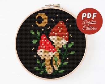 Op de afbeelding: Een kruissteekpatroon met twee rode en witte paddenstoelen met gouden stelen en groene bladeren op een zwarte achtergrond met een halve maan en sterren.