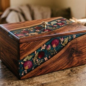 Puede incluir: Caja de madera con acabado oscuro, con incrustaciones decorativas de flores secas y resina color turquesa. La caja tiene un pomo dorado y est&aacute; colocada sobre una superficie de madera. Un ramo de flores secas est&aacute; en el fondo.