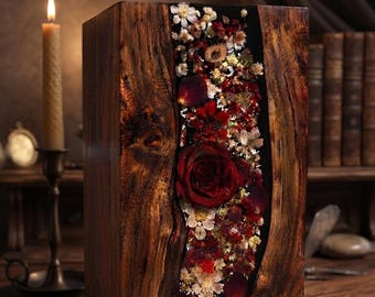 Peut inclure: Un bloc de bois rectangulaire avec une incrustation verticale centrale de fleurs séchées encapsulées dans de la résine transparente. Le bois présente une finition sombre et polie avec des veines apparentes et une rose rouge centrale.