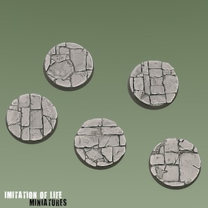 Pode incluir: Cinco bases circulares cinzentas em miniatura com textura de pedra. Cada base é feita de peças de pedra individuais, criando um efeito de calçada. As bases estão dispostas sobre um fundo verde. O texto "IMITATION OF LIFE MINIATURES" está na parte inferior.