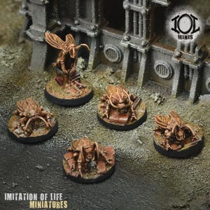 Op de afbeelding: Miniatuurbeeldjes van insectachtige wezens met vleugels en gedetailleerde exoskeletten. De figuren zijn geschilderd in bruin- en beigetinten, gemonteerd op ronde bases. De miniaturen staan tegen een achtergrond van een verweerde, industrieel gethematiseerde omgeving. De tekst "IMITATION OF LIFE MINIATURES" staat onderaan.