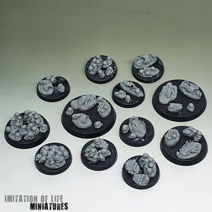 May include: A collection of miniature bases, each with a black circular base. The bases are adorned with gray skeletal remains, including skulls and rib cages. The bases vary in size and the arrangement of the skeletal elements.