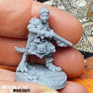 Può includere: Una miniatura grigia di un personaggio fantasy, con un fucile. La figura ha occhiali, spalline a punta e una coda. La base è strutturata. Il testo "IMITATION OF LIFE MINIATURES" è in basso.