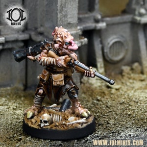 Peut inclure: Figurine miniature d'une créature ressemblant à un gobelin tenant un fusil, peinte dans des tons de marron, beige et rose. La figurine est posée sur un socle avec un crâne et des os, sur fond de ruines. Le logo "101 MINIS" est visible.