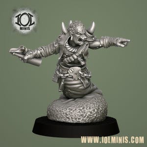 Puede incluir: Miniatura plateada de una criatura fantástica con cuernos, chaqueta y cuerpo inferior de serpiente. La figura posa con un brazo extendido, señalando, y el otro sosteniendo un arma. La base es negra y la dirección del sitio web es visible.