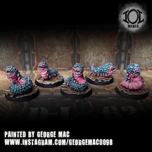 May include: Five miniature figurines of worm-like creatures with open mouths and sharp teeth. The creatures are painted in pink and blue, mounted on small, round bases. The image includes text at the bottom: "PAINTED BY GEORGE MAC" and a website address.