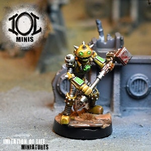 May include: A miniature robot figure with a yellow and silver color scheme, holding a hammer. The robot has green accents and is posed on a small, round base. The figure is set against a blurred background with the text "101 MINIS" and "IMITATION OF LIFE MINIATURES".