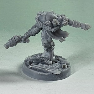 Può includere: Una figura in miniatura grigia di un guerriero futuristico, con armatura dettagliata, un'arma in una mano e un pugno chiuso. La figura è montata su una base strutturata, che suggerisce una scena di battaglia. Il design generale è intricato e dettagliato.