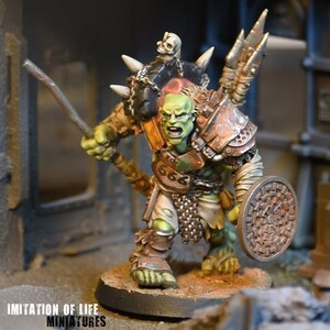 Può includere: Figura in miniatura di un guerriero orco dalla pelle verde, con lancia e scudo. L'orco indossa un'armatura e ha un teschio sulla spalla. La figura è dipinta con dettagli e montata su una base circolare.