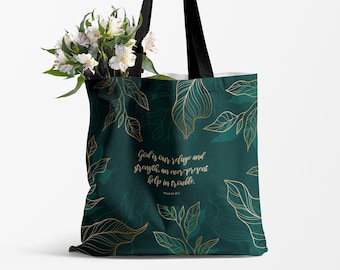 May include: A tote bag with a dark teal background and gold leaf design. The bag has black handles and contains white flowers. Text on the bag reads "God is our refuge and strength, an ever present help in trouble."