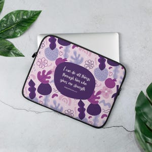 Puede incluir: Funda para portátil con un estampado floral en tonos morados y rosas. El diseño incluye flores estilizadas, hojas y formas abstractas. Un óvalo central contiene el texto "Todo lo puedo en Cristo que me fortalece" de Filipenses 4:13.
