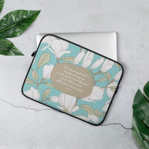 Puede incluir: Funda para portátil con un diseño floral con flores de magnolia blancas y hojas verdes sobre un fondo azul claro. La funda tiene una cremallera negra y una cita en un óvalo marrón. El texto dice: "¿No te lo he ordenado yo? ¡Sé fuerte y valiente! No temas ni desmayes, porque el Señor tu Dios estará contigo dondequiera que vayas."