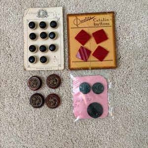 以下が含まれることがあります： クリーム色の縁取りがある11個の丸い黒いボタンの台紙、Quality Catalin buttonsと書かれた4個の赤いひし形のボタンの台紙、金色の花模様の中心を持つ4個の丸い茶色のボタン、そして3個の暗い色のボタンを含むヴィンテージボタンのコレクション。