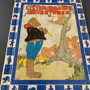 Op de afbeelding: Vintage kinderboek getiteld "Little Bear's Adventures". De omslag toont een beer die fluit speelt, eekhoorns en een blauwe rand met berensilhouetten. Het boek heeft slijtage.