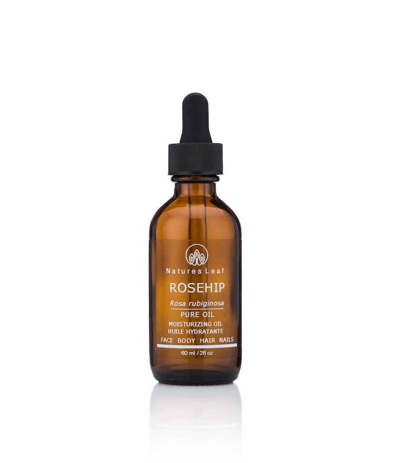 May include: A brown glass bottle with a dropper top containing rosehip oil. The bottle is labeled "Natures Leaf Rosehip Rosa rubiginosa Pure Oil Moisturizing Oil Huile Hydratante Face Body Hair Nails 60 ml / 2 fl oz."