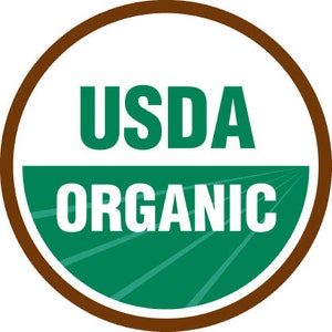 Op de afbeelding: Een bruine cirkel met een witte achtergrond en groene tekst. De tekst luidt "USDA ORGANIC".