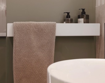 May include: A modern bathroom scene featuring a white sink and a white shelf holding two dark soap dispensers. A beige towel hangs from the shelf. The wall is painted a muted green, creating a spa-like atmosphere.