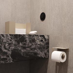 Puede incluir: Una escena de ba&ntilde;o moderno con una encimera de m&aacute;rmol negro y gris, una caja de pa&ntilde;uelos y jab&oacute;n. Un rollo de papel higi&eacute;nico est&aacute; montado en la pared. Las paredes son de color beige claro.