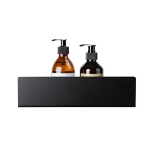 May include: A matte black rectangular metal wall shelf holding two amber glass bottles with black pump dispensers. The shelf features a solid front panel and a flat surface for storage, providing a clean and functional display for liquid containers.