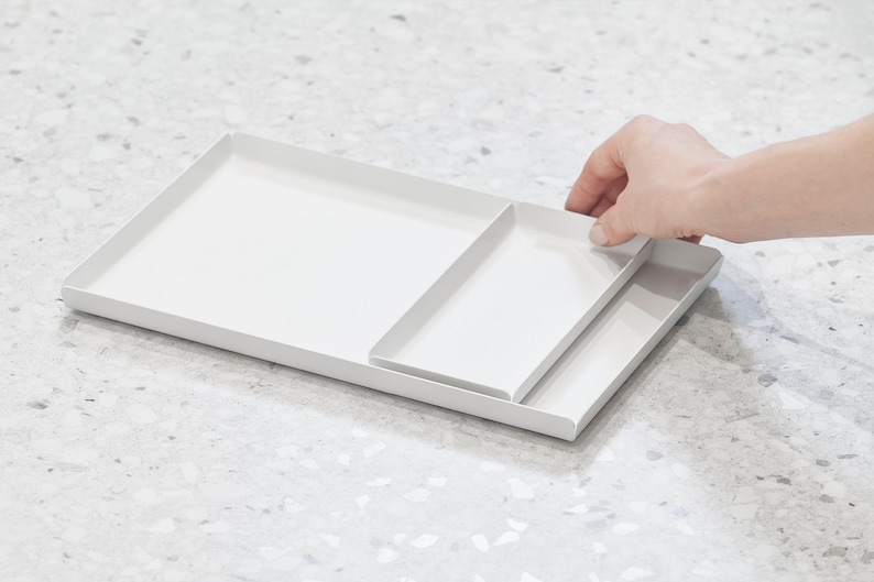 May include: A white metal tray with a smaller white metal tray inside. The trays are nested together and have a modern, minimalist design.