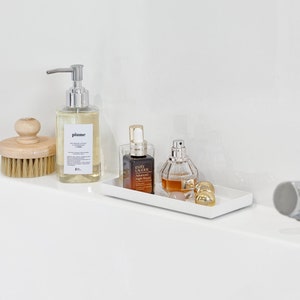 May include: A white rectangular tray with three bottles of liquid. The bottles are clear glass with gold accents. The tray is sitting on a white countertop.