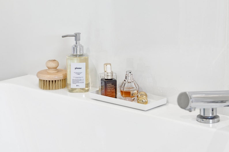 May include: A white rectangular tray with three bottles of liquid. The bottles are clear glass with gold accents. The tray is sitting on a white countertop.