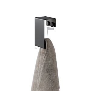May include: A matte black metal over-the-door hook featuring a flat rectangular front panel and two small circular knobs on the inner side, with a folded light brown textured towel draped over the lower section of the hook structure.