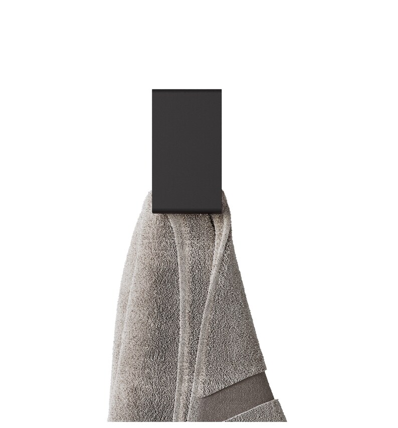 May include: A matte black rectangular wall hook holding a folded light gray towel. The hook features a flat, vertical design with a curved bottom edge, while the towel displays a soft, textured fabric surface with a visible hemmed border detail.