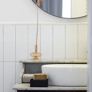 May include: A white porcelain sink with a brown bar of soap in a black soap dish on a marble countertop. A dried flower arrangement is in a clear glass vase on the countertop.