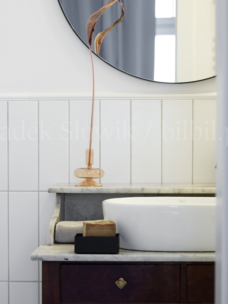 May include: A white porcelain sink with a brown bar of soap in a black soap dish on a marble countertop. A dried flower arrangement is in a clear glass vase on the countertop.