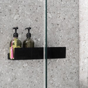 May include: Two clear glass bottles with black pump tops and pink tassels, sitting on a black shelf in a shower.