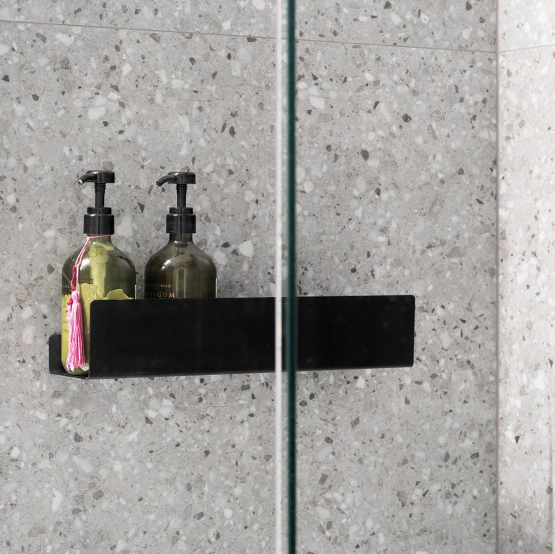 May include: Two clear glass bottles with black pump tops and pink tassels, sitting on a black shelf in a shower.