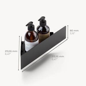 May include: A matte black triangular corner shelf holding two amber glass pump bottles. The shelf measures 8.47 inches along the two back sides and 3.15 inches in height. The design features a solid metal construction with a front-facing panel.
